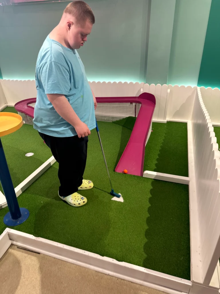 Adult member putting on an indoor mini golf course during a community outing.