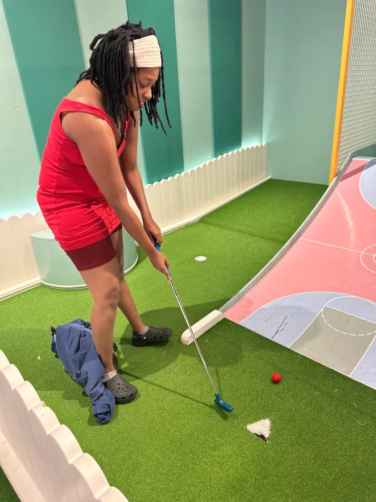 Adult member playing indoor mini golf during a community outing with an adult day support program.