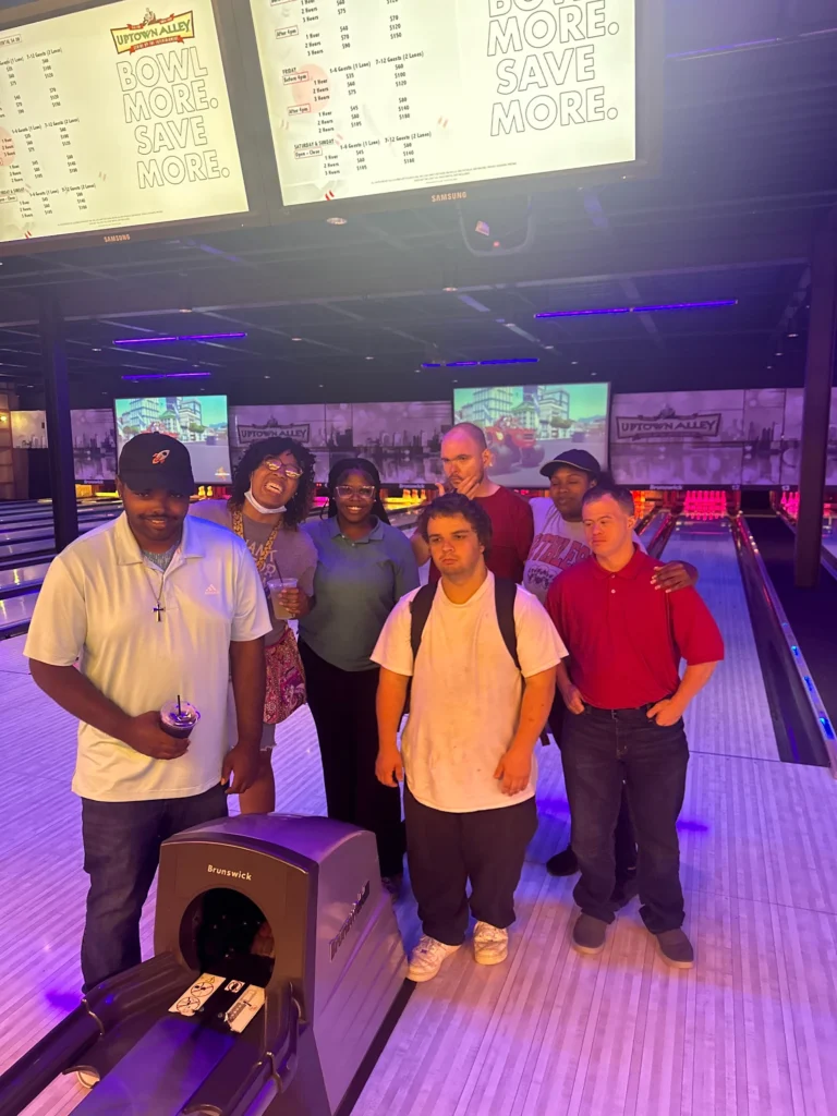 Adults posing together at a bowling alley during a community outing with an adult day support program.