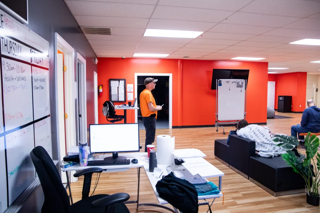 Activity room with a weekly schedule board, staff workstation, and adults during an adult day support program.