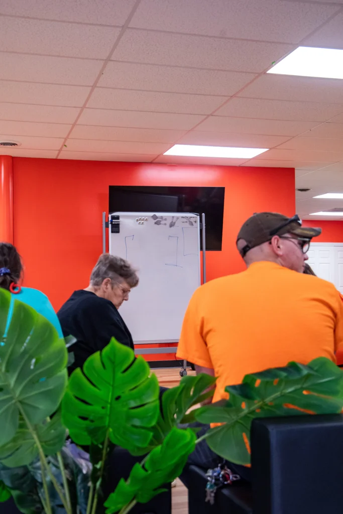 Adults seated near a whiteboard during a quiet group learning activity at an adult day support program.