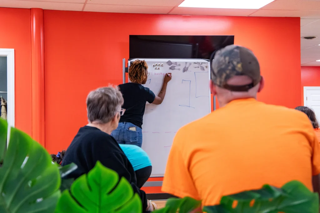 Staff member writing on a whiteboard while adults listen during a learning activity at an adult day support program.
