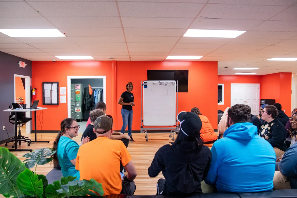 Staff member leading a community engagement group session with adults seated together at an adult day support program.