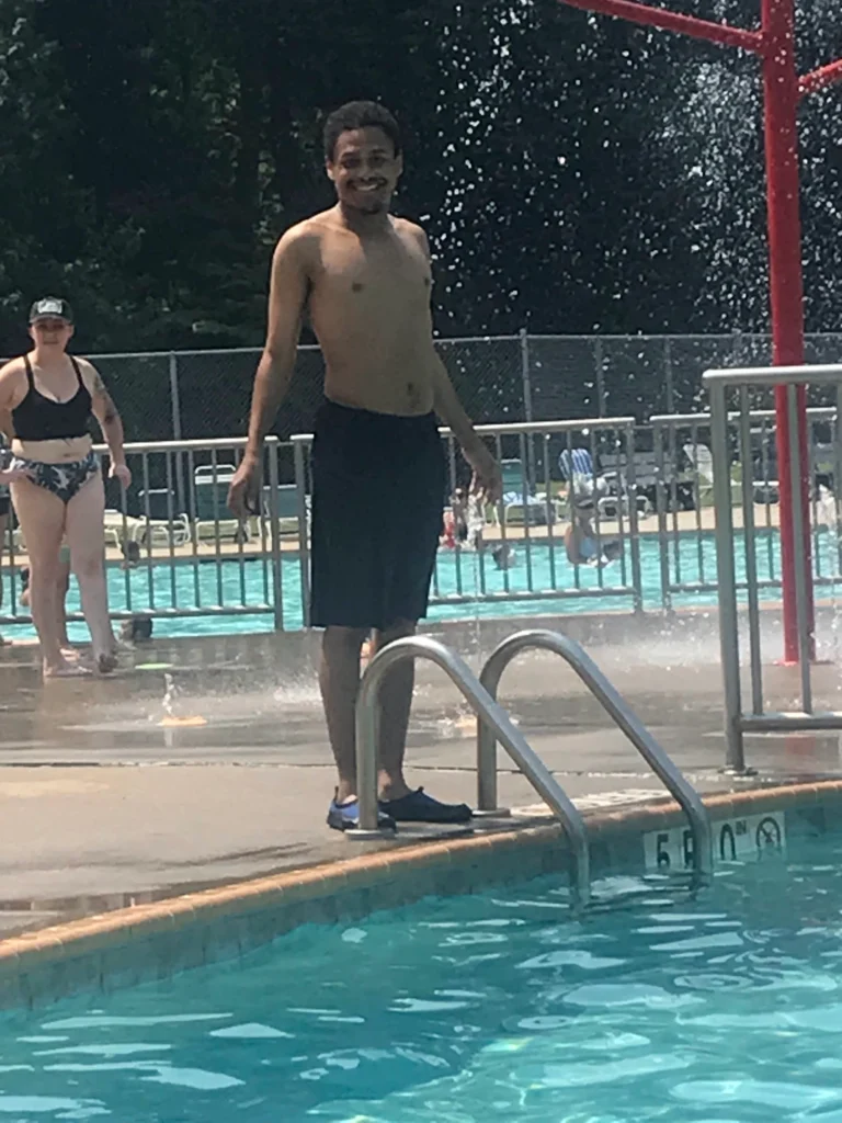 Adult member standing by the pool during an outdoor community outing with an adult day support program.
