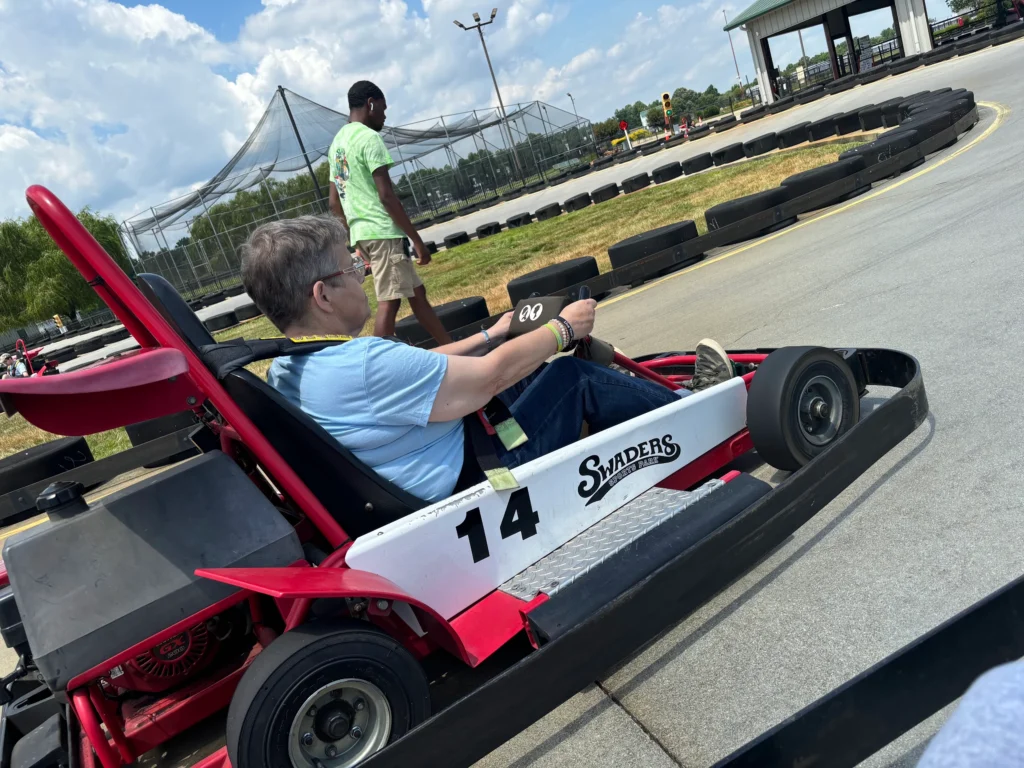 Adult member driving a go-kart on an outdoor track during a community engagement outing.