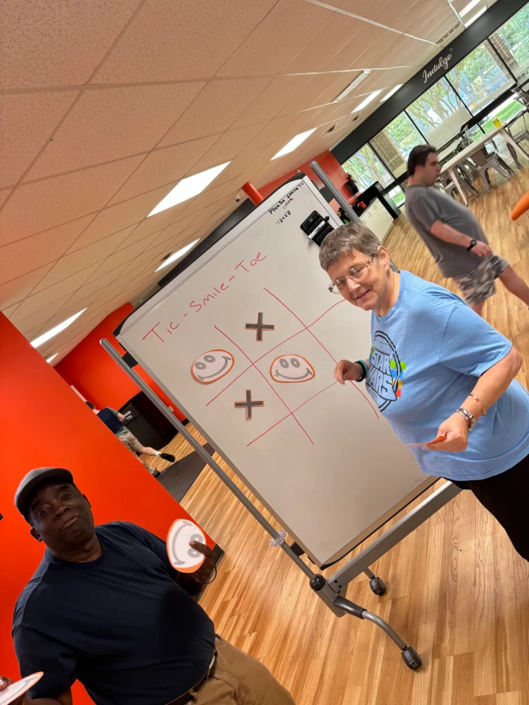 Adults playing a tic-tac-toe style game on a whiteboard during an adult day support program activity.