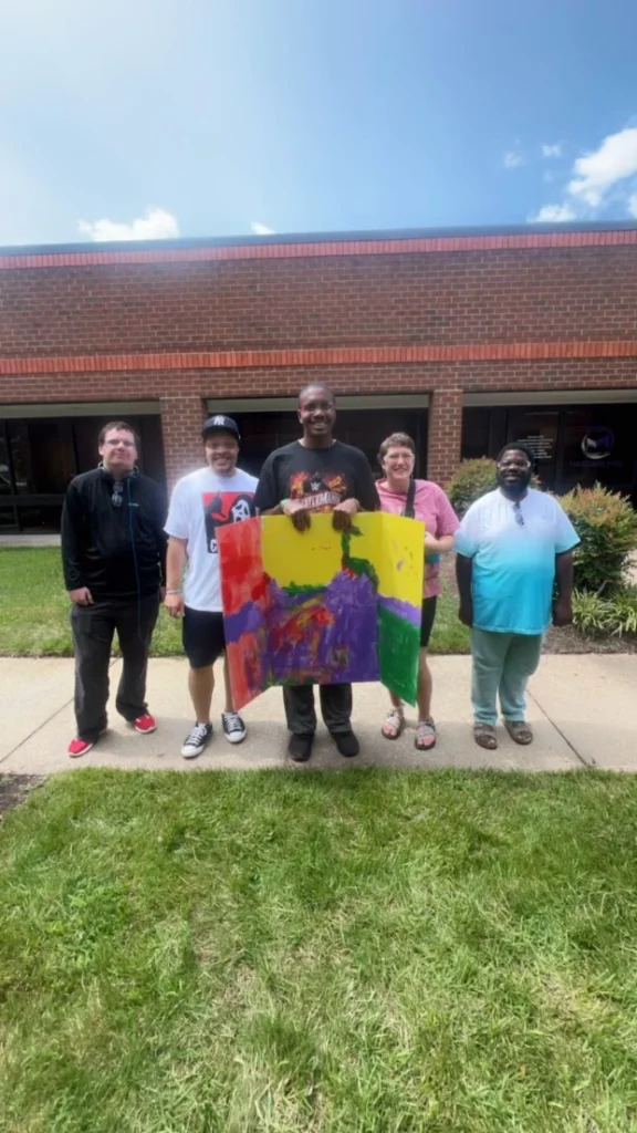Adults standing outside together with a colorful art project during an adult day support program activity.