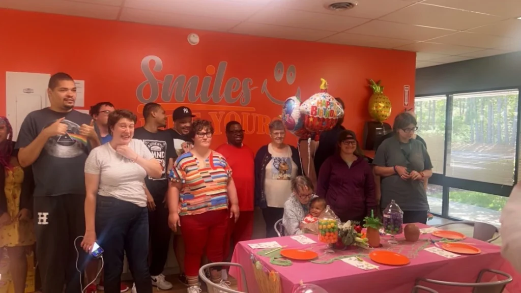 Adults and staff gathered around a birthday table during an adult day support program celebration.