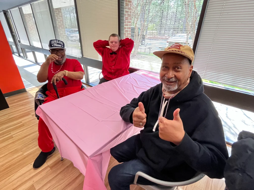 Adult members smiling and giving thumbs up during a table social activity at an adult day support program.