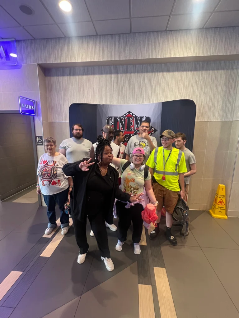 Adults and staff posing together during a movie theater community outing with an adult day support program.