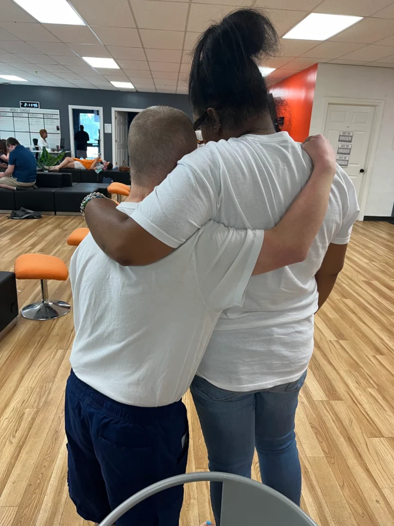 Two adults standing with arms around each other in a supportive adult day support program setting.