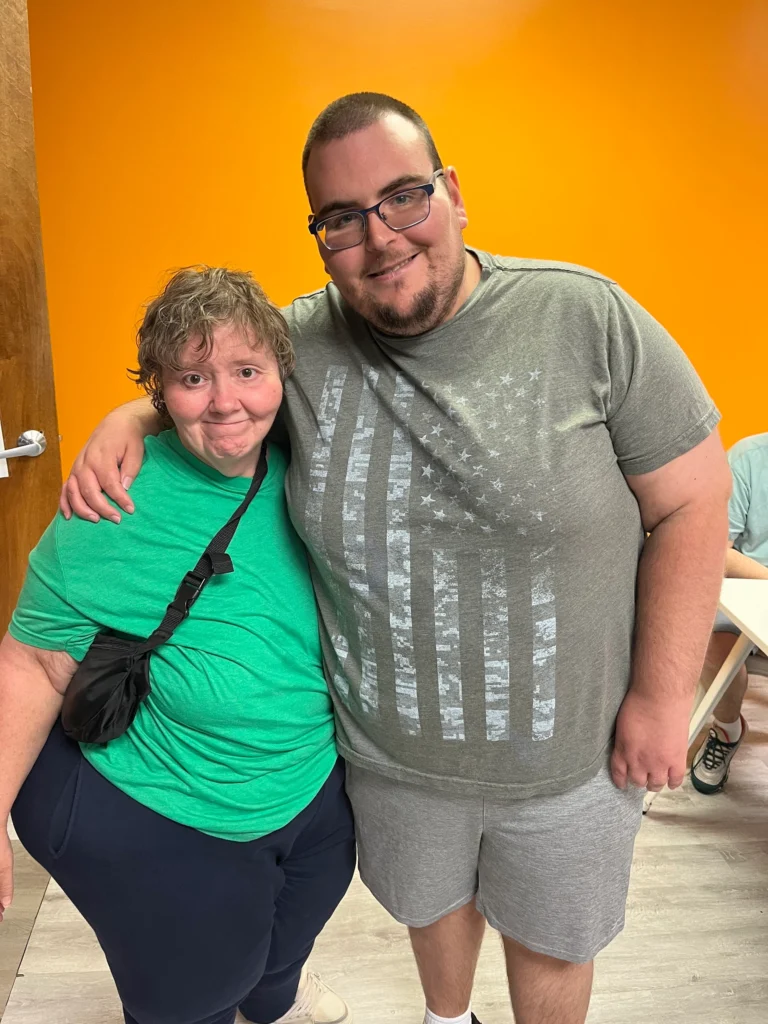 Two adult members standing together and smiling during an adult day support program activity.