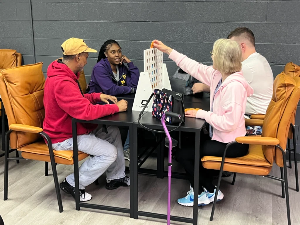 Adults playing Connect Four together at a table during an adult day support program activity.