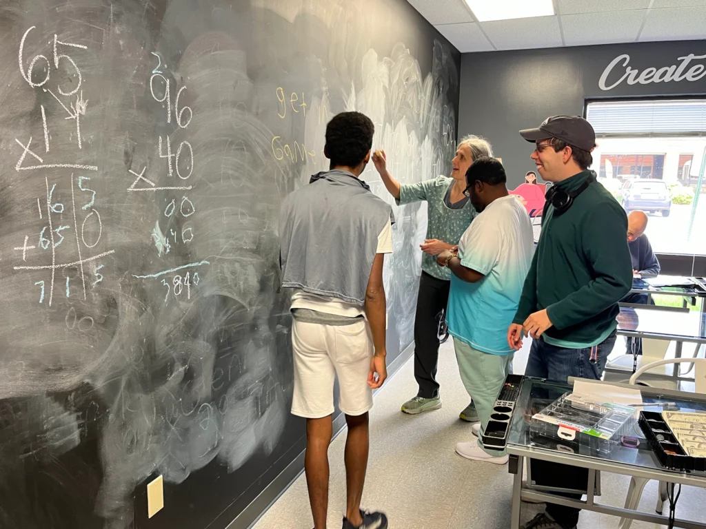 Adults and staff working together at a chalkboard during a learning activity at an adult day support program.