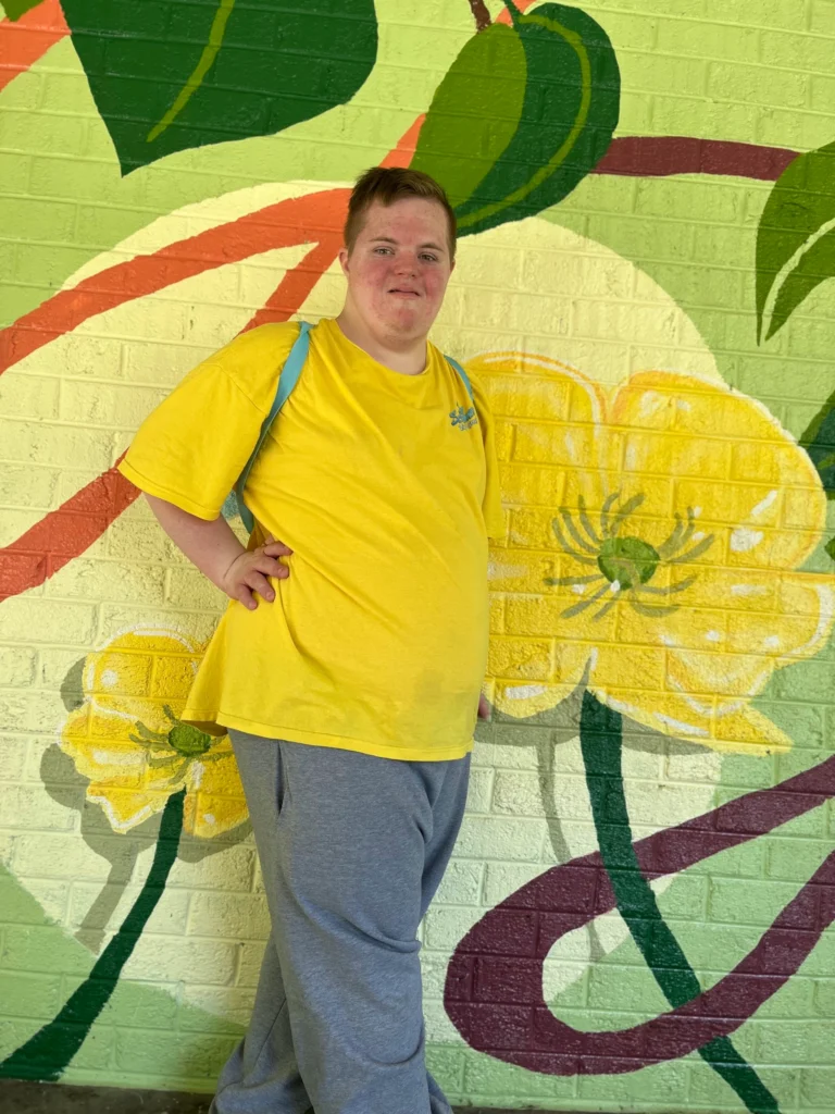 Adult member posing in front of a colorful flower mural during a community outing.