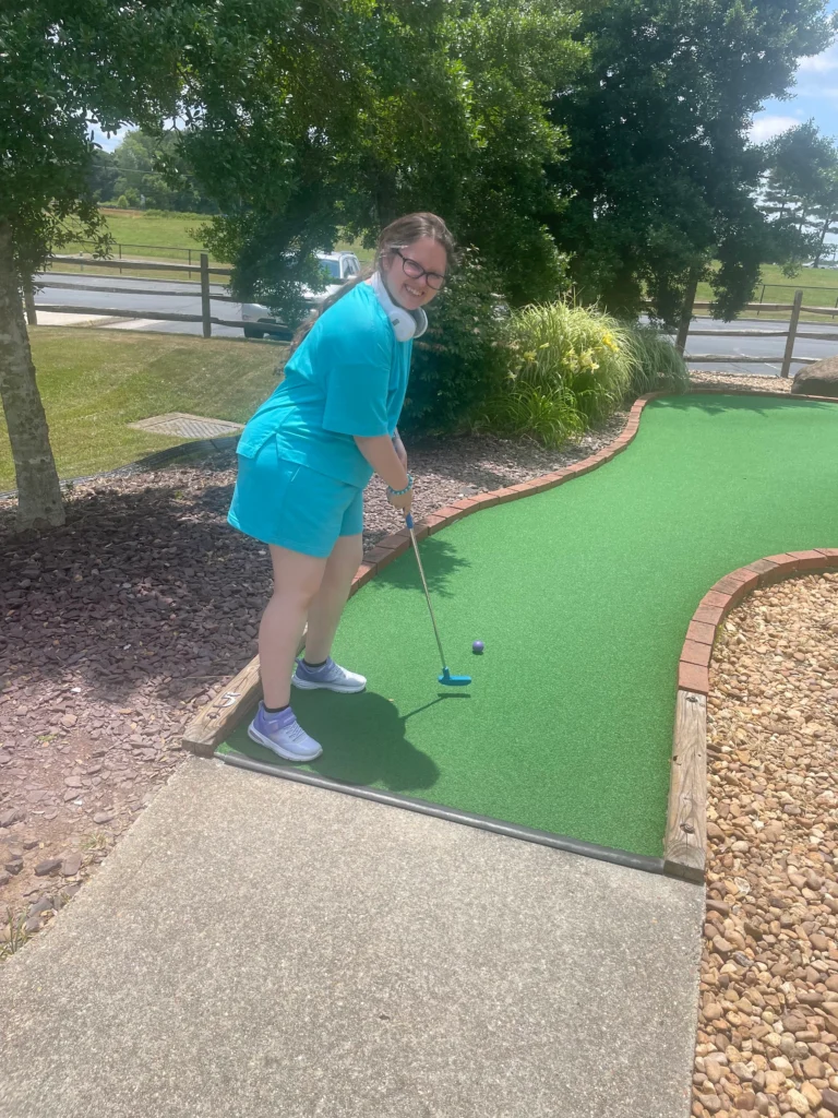 Adult smiling while playing mini golf during an outdoor community engagement activity.