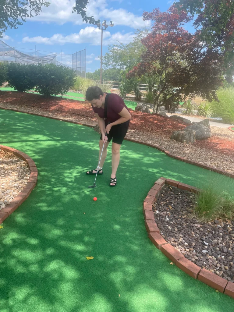 Adult playing mini golf outdoors during a community outing with an adult day support program.