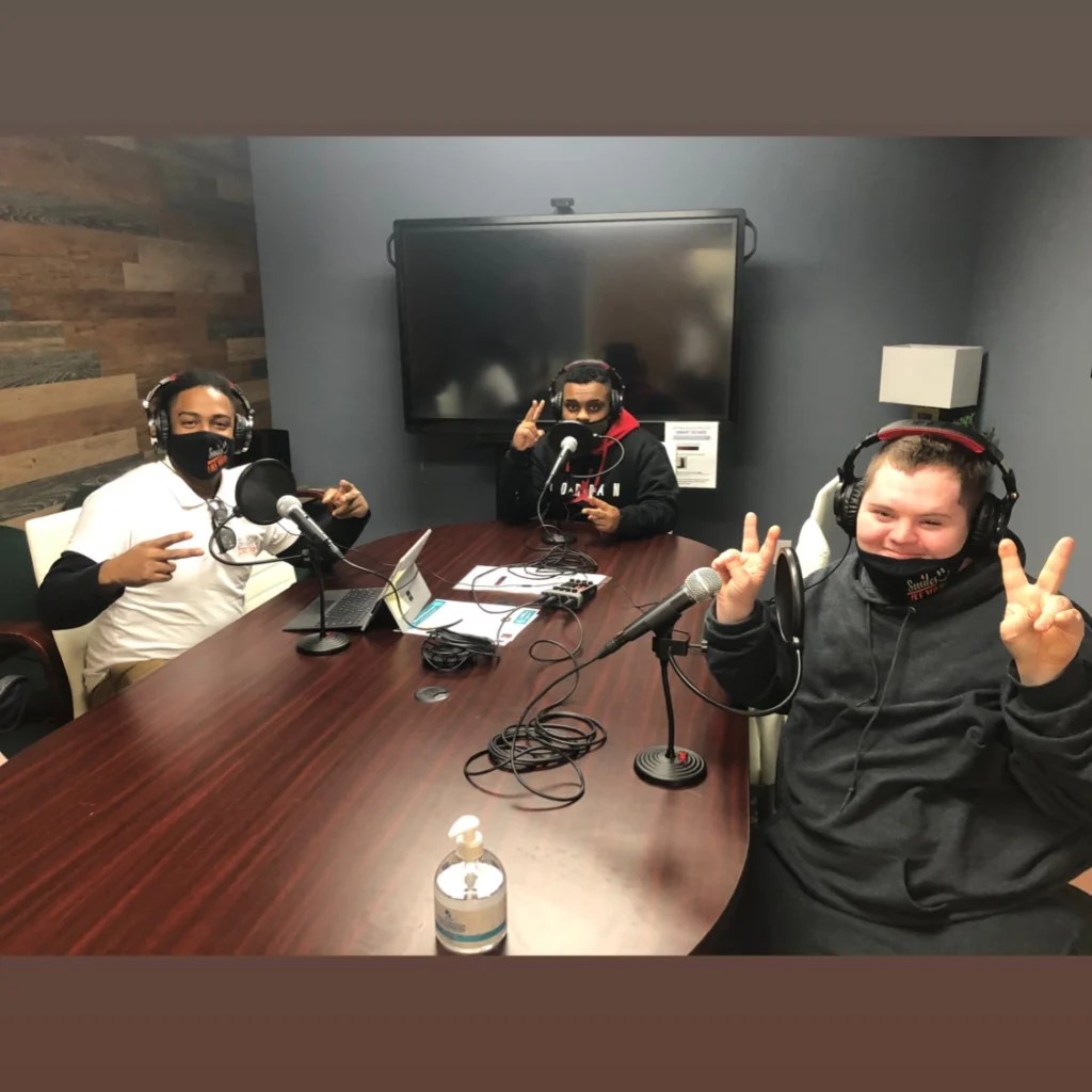 Adults and staff wearing headphones and speaking into microphones during a podcast recording activity.