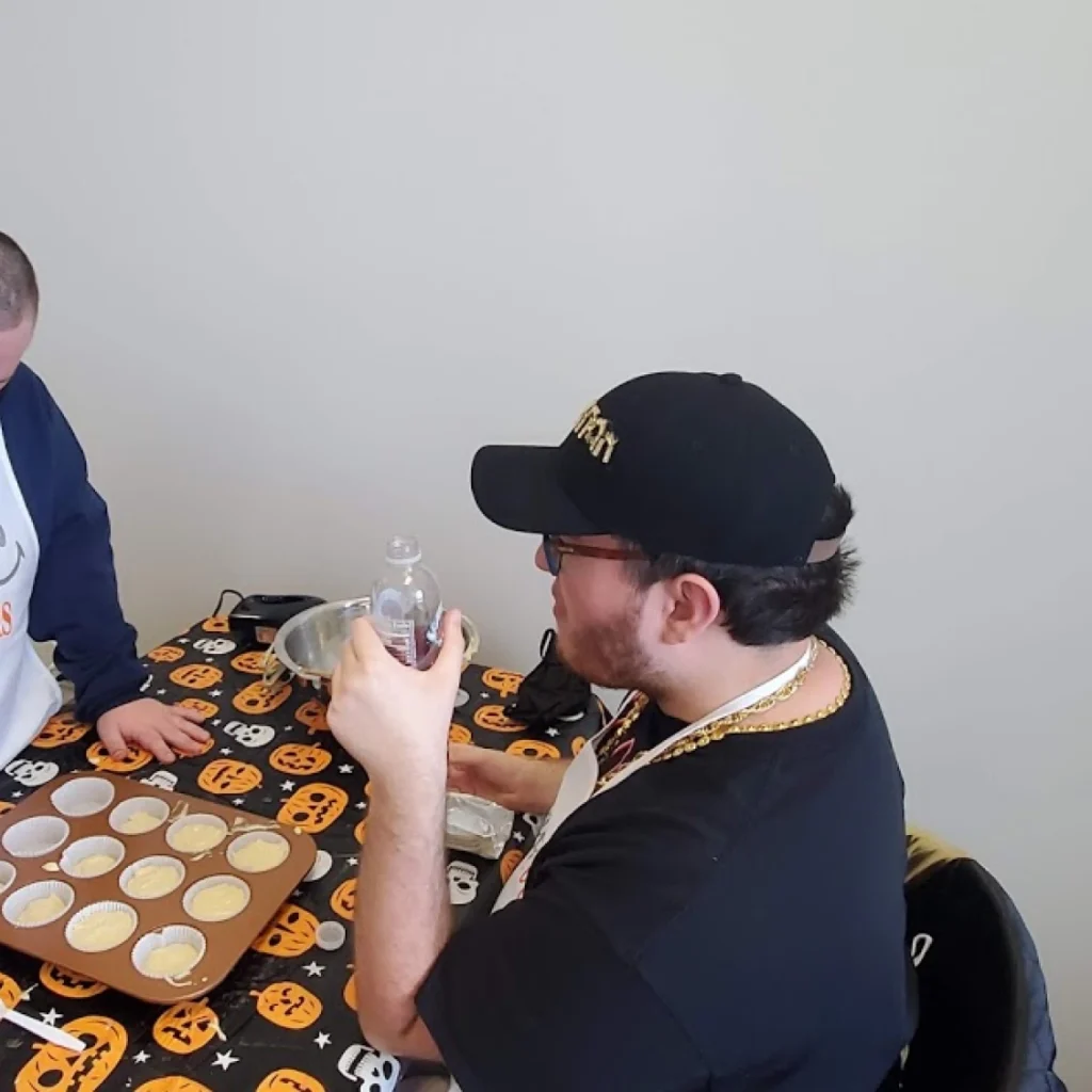 Adult member and support staff preparing cupcake batter during a cooking activity at an adult day program.