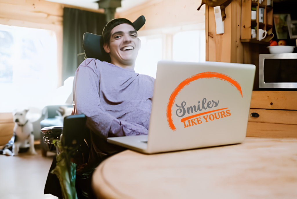 Wheelchair user smiling while using a laptop at home.