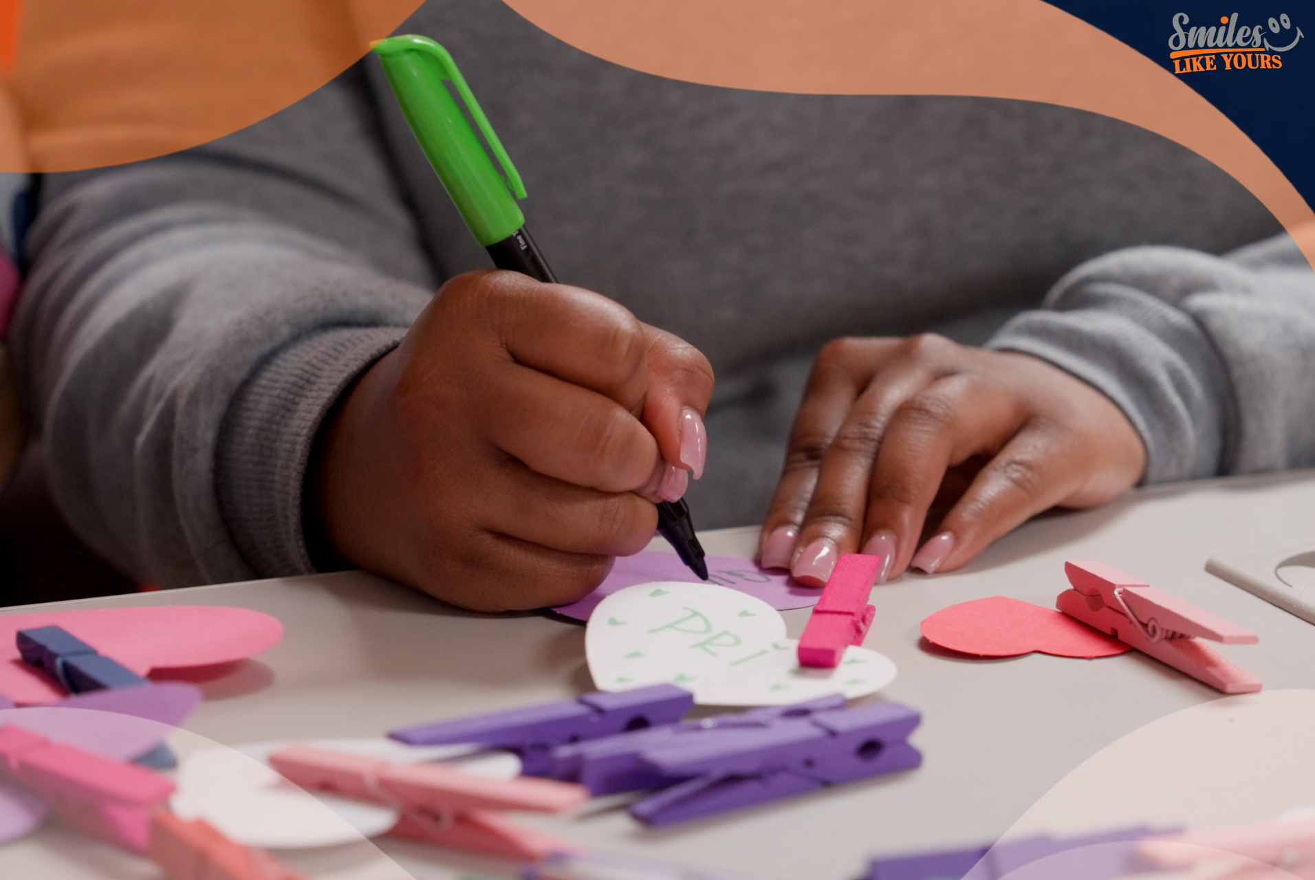 Person writing on a paper heart during a Smiles Like Yours activity.