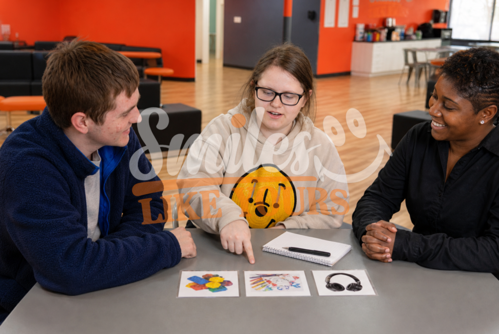 Adult woman choosing between visual activity options with support from a peer and a Smiles Like Yours staff member.