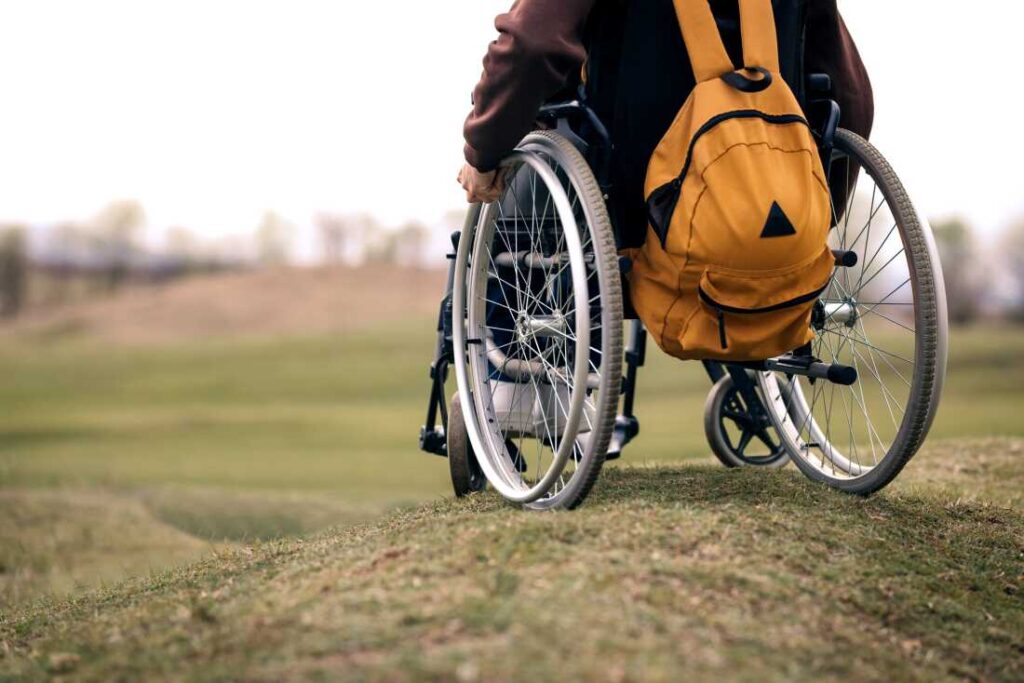 Wheelchair user outdoors carrying an orange backpack on a grassy path