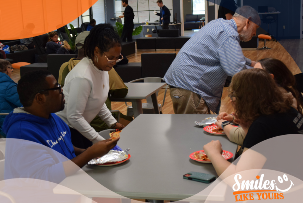 Adults with developmental disabilities and support staff sharing a meal at the Smiles Like Yours community center.